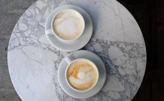 Two cups of cappuccino or latte decorated with foam on marble table background in Coffee shop. Morning coffee for couple in love. Top view. Two white mugs of coffee. photo