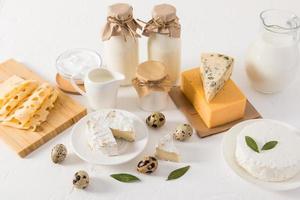 un conjunto de productos naturales frescos: leche, requesón, queso, crema agria y huevos en varios platos sobre una mesa blanca contra una pared de ladrillo blanco. foto