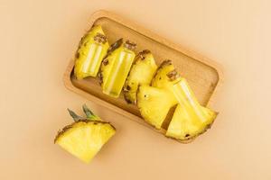 glass bottles with a cork with pineapple cosmetic lie on juicy pineapple slices and a wooden tray. top view. brown background. photo