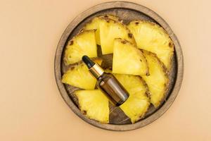 serum for facial skin care with pineapple extract lies on ripe pineapple slices and a wooden tray. top view. brown background. photo