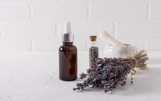 serum with an extract of lavender herbs for face and body skin care in a glassbottle on a white table and the brick wall. photo