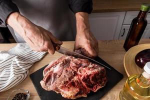 the butcher's hands cut a fresh piece of beef on an slate board and a wooden table with a sharp chef's knife. eco products from your own farm.