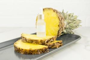 a brightening serum with pineapple extract in a cosmetic white bottle with a pipette stands onpineapple slices. natural cosmetics. Unbranded mock-up. photo