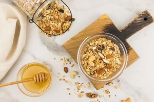 baked granola or muesli with nuts, dried fruits and honey in a glass bowl on a wooden board. top view. marble background. photo