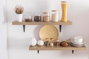 open wooden shelves with various glass jars with a wooden lid filled with spices, coffee, spaghetti. stylish decor in the modern kitchen. front view. photo