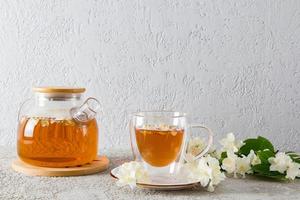 front view of a glass teapot with jasmine tea and a modern cup with a natural delicious drink. gray background. tea time. photo