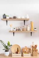 Open kitchen wooden shelves with jars for storage on a white textured wall and part of the countertop with environmentally friendly items for storage. photo