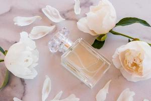 beautiful composition with an elegant perfume bottle and white peonies on a marble background. the concept of perfumery and beauty. photo