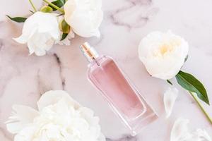 un patrón de perfume o agua de tocador sobre un fondo blanco de mármol entre peonías fragantes blancas. concepto publicitario de perfumes femeninos. foto