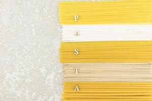 la vista superior de la pasta italiana seca, fideos, espaguetis sobre un fondo gris con una copia del espacio y las letras de la palabra - pasta. endecha plana foto