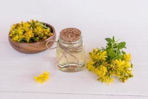 a bottle with healing natural St. John's wort oil on a white wooden background with the flowers of the plant. the concept of alternative medicine. photo