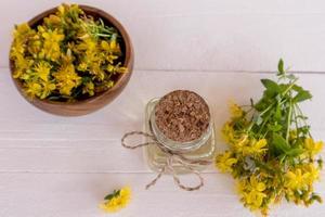 Top view of a bottle of organic St. John's wort oil, a wooden bowl with plant flowers and a bouquet. natural medicinal plants. Selective focus. photo