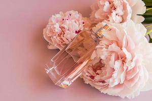 an elegant bottle of women's perfume or toilet water on a pink background with a beautiful peony . top view. a copy of the space. photo