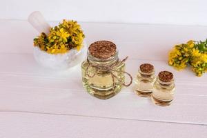 glass bottles of organic St. John's wort oil stand on a table of white wooden boards. mortar and pestle with grass flowers. alternative medicine. photo