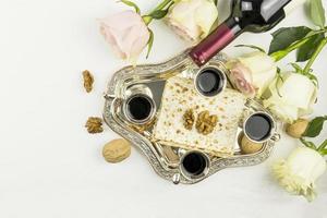 top view of a silver tray with matzah, walnuts and red wine in silver glasses. roses on a white background. the concept of the Jewish Passover . photo