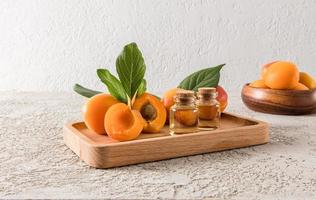 bottles of apricot oil on a wooden tray among ripe apricots. soothing care. skin restoration. gray cement background. photo