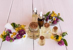 un conjunto de aceites cosméticos, orgánicos y esenciales en varias botellas sobre una mesa de madera blanca con plantas medicinales de pradera. enfoque selectivo. foto