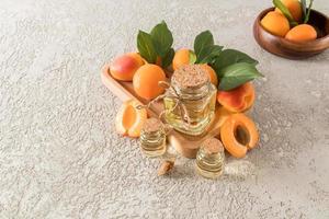 three different bottles of apricot oil on a wooden tray among ripe apricots. soothing care. skin restoration. gray cement background. photo