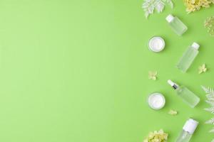 Cosmetic skin care products with with flowers on green background. Flat lay, copy space photo