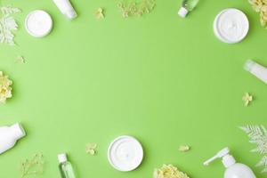 Cosmetic skin care products with with flowers on green background. Flat lay, copy space photo