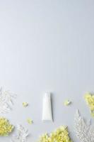 White tube of cosmetic cream with flowers on grey background. Flat lay, copy space photo