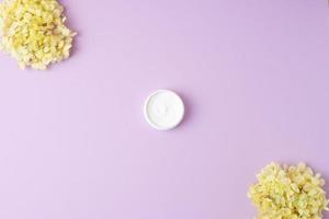 Jar of cosmetic cream with flowers on rose background. Flat lay, copy space photo