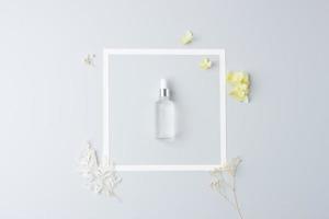 Cosmetic bottle with flowers and white frame on grey background. Flat lay, copy space photo