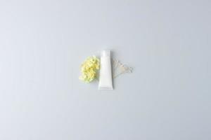 White tube of cosmetic cream with flowers on grey background. Flat lay, copy space photo
