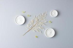 Jars of cosmetic cream with flowers on grey background. Flat lay photo