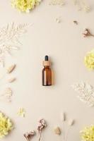 Cosmetic bottle with flowers on pastel beige background. Flat lay photo