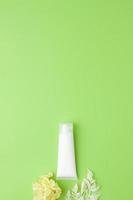 tubo blanco de crema cosmética con flores sobre fondo verde. endecha plana, espacio de copia foto