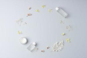 Minimal composition with cosmetic skin care products and flowers on grey background. Flat lay, copy space photo