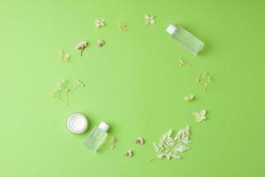 Minimal composition with cosmetic skin care products and flowers on green background. Flat lay, copy space photo