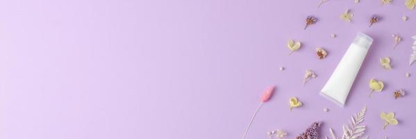 tubo blanco de crema cosmética con flores sobre fondo rosa. endecha plana, espacio de copia foto