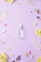 Cosmetic bottle with flowers on rose background. Flat lay photo