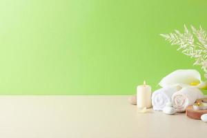 Spa treatment with candles, towel and flowers on green background. Close up, copy space photo