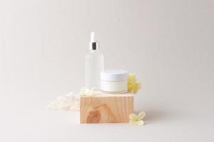 Cosmetic skin care products with wood podium and flowers on grey background. Close up, copy space photo