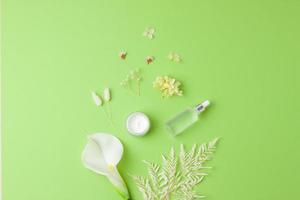 Cosmetic skin care products with flowers on green background. Flat lay, copy space photo