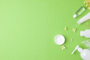 Cosmetic skin care products with with flowers on green background. Flat lay, copy space photo