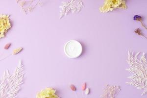 Jar of cosmetic cream with flowers on rose background. Flat lay photo