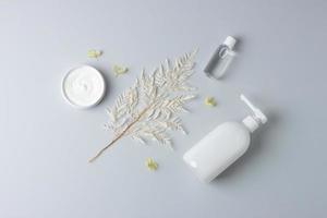 Cosmetic skin care products with flowers on grey background. Flat lay photo