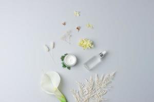 Cosmetic skin care products with flowers on grey background. Flat lay, copy space photo