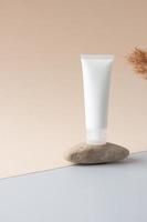 White tube of cosmetic cream on a stone podium with pampas on beige background. Close up. photo