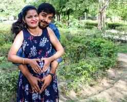 Indian couple posing for maternity baby shoot. The couple is posing in a lawn with green grass and the woman is falunting her baby bump in Lodhi Garden in New Delhi, India photo