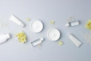 Cosmetic skin care products with with flowers on grey background. Flat lay, copy space photo