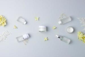 Cosmetic skin care products with with flowers on grey background. Flat lay, copy space photo