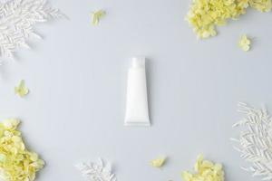 tubo blanco de crema cosmética con flores sobre fondo gris. endecha plana, espacio de copia foto