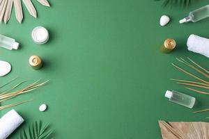 Spa treatment with cosmetic bottle, candles and palm leaf on green background. Flat lay, copy space photo