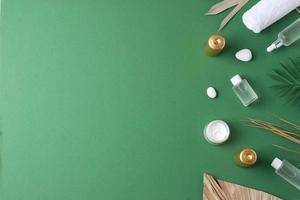 Spa treatment with cosmetic bottle, candles and palm leaf on green background. Flat lay, copy space photo