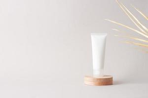 White tube of cosmetic cream with wood podium and palm leaf on grey background. Close up, copy space photo